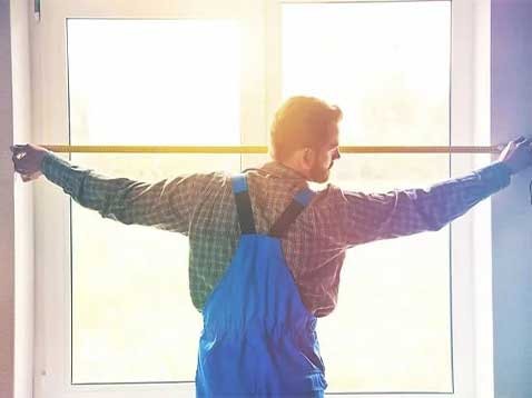 Man in overalls measuring a window with a tape measure